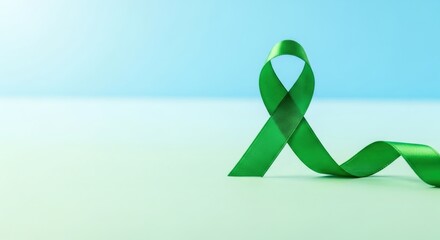 Green awareness ribbon on a clear light blue background with copy space. Symbol for mental health, organ donation, or Celiac Disease awareness.