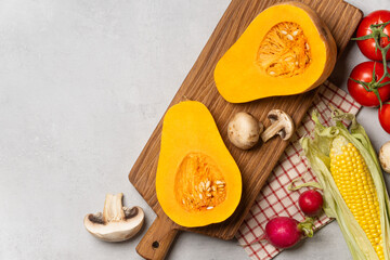 Fresh autumn harvest with pumpkins, corn, mushrooms, and colorful fall leaves on a gray background.