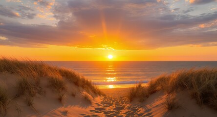 Sunset over ocean viewed through sandy dunes with soft clouds  