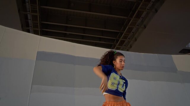 Arc shot of talented gen Z biracial girl in streetwear performing modern dance under urban bridge at daytime expressing her individuality and passion
