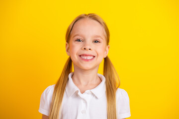 Cheerful schoolgirl smiling against a vibrant yellow background symbolizing youthful energy and...