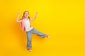 Cheerful schoolgirl on a bright yellow background wearing casual style clothing and posing happily...