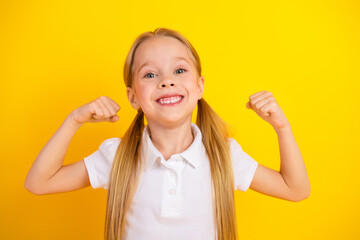 Happy schoolgirl celebrating success with enthusiastic expression standing on vibrant yellow...