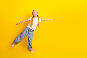 Cheerful schoolgirl in casual outfit proudly posing against a vibrant yellow background in a...