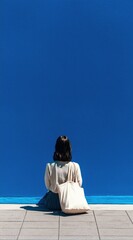 Person sitting by a blue wall on a sunny day, contemplating life in a peaceful setting