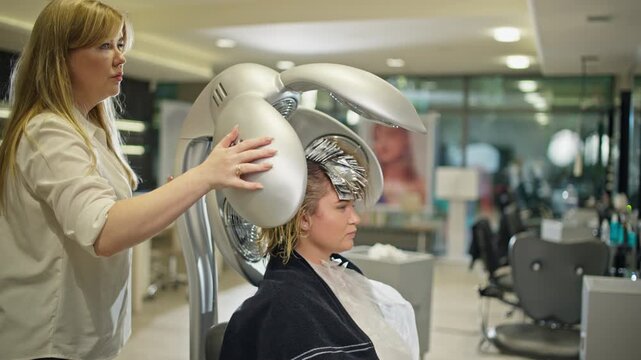 Hairdresser inserts a hair straightener to speed up the hair coloring process. Woman undergoing beauty treatments in a beauty salon.