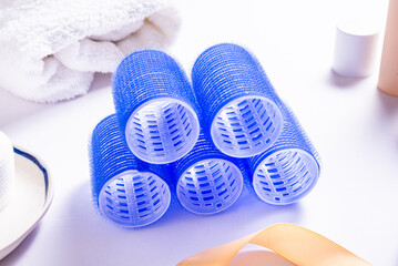 Set of Blue Plastic Hair Rollers with Hair Care Products on White Table