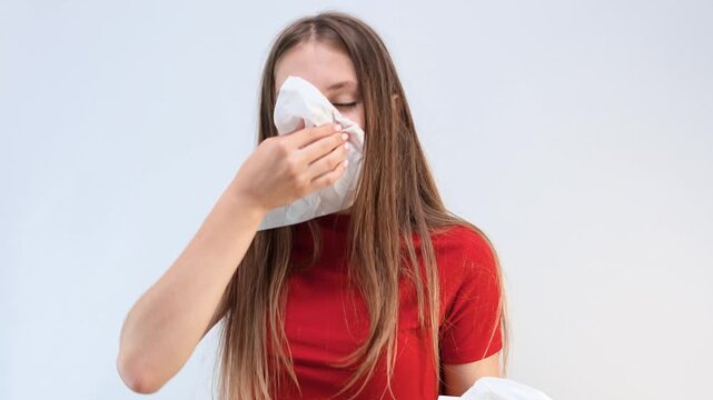 Young teen girl blows her nose and sneezes into a paper napkin on an isolated background, the concept of illness and seasonal colds or allergies