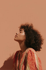 Young woman with curly hair enjoying sunlight against terracotta wall