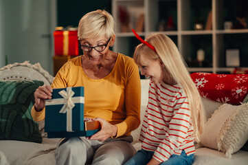 Grandmother opening christmas gift with granddaughter smiling