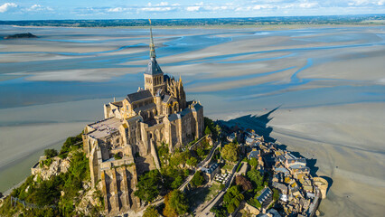Aerial view of Mont Saint Michel in Normandy, France, during low tide, showing the iconic abbey rising above the sandy bay, a UNESCO World Heritage site and popular tourist destination