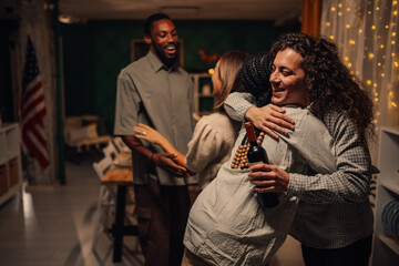 Friends embracing at thanksgiving dinner party, celebrating with wine and warmth