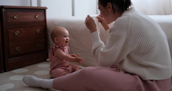 Slow-motion shot of a mother playing peekaboo with her infant daughter while sitting together on the bedroom floor.