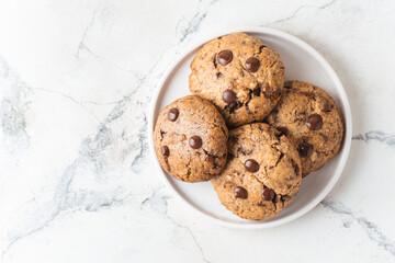 Stack of fresh chocolate American style chip cookies with nuts and chocolate drops on white marble background. Flat lay of cookies with peanut butter filling inside