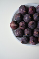 Minimalist food styling with a fresh purple fig and a bowl of ripe figs on a clean white background. Modern composition perfect for cookbooks, blogs, and wellness projects.