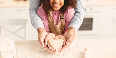 Happy Loving Family. Smiling african american little girl and her father holding dough in heart shape in hands, daddy and daughter having fun at kitchen, baking cake. Celebrating Father's Day