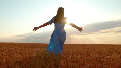 Young girl joyfully runs through wheat field at sunset. Concept of woman's dream in nature. Female farmer, arms outstretched, runs through wheat field. Happy, free woman runs through ears of wheat © Victoriia