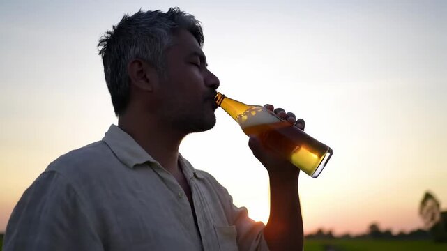 Man drinking beer at sunset in a field