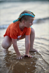 Girl plays in the sea water at sunset