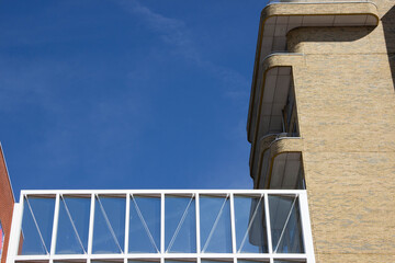Obraz premium Modern architectural building with a glass bridge connecting two structures against a clear blue sky, showcasing contemporary design and urban aesthetics