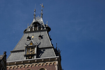 Obraz premium Architectural detail of a historic clock tower with intricate design elements, featuring a slate roof, decorative spires, and a clear blue sky backdrop, showcasing timeless craftsmanship
