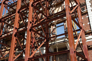Steel framework of a building under construction, showcasing intricate structural design and exposed brickwork, with clear blue sky in the background, representing modern architecture and engineering