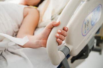 Close-up of a patient's hand holding the bed rail in a hospital room, conveying a sense of vulnerability and the need for support during medical care