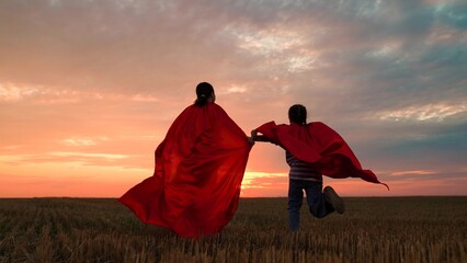Happy children run across meadow in red superhero capes. Little girls in red capes play superheroes...