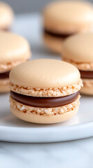 Close-up of a golden-colored macaron filled with rich chocolate ganache, sitting on a white plate, showcasing its delicate texture and inviting appearance.