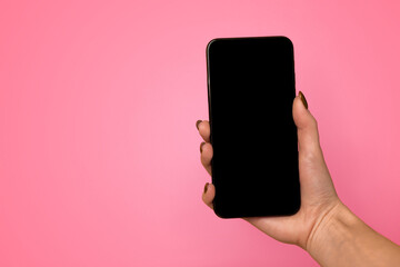 Technology concept. Female hand holding smartphone with black blank screen for mockup on yellow studio background with free space, browsing information or social media, using application, top view