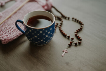 Rosary with cross beside coffee mug and knitting on table