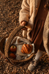 A person holding a picnic basket with apples and a croissant.