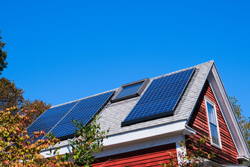 Solar panels on a rustic countryside house roof under a clear blue sky, showcasing clean energy and sustainable living. © Veronique