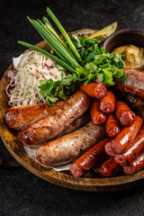 Grilled sausages with fresh herbs and mustard on wooden plate.