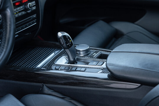 Automatic gear selector in luxury car. Automobile interior in dark tones, bottom part of center console with lots of buttons.
