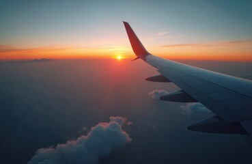 Fototapeta premium View from airplane window at sunrise above clouds. Aircraft wing, sun disk low on horizon, orange sky, dawn light. Peaceful flight journey over atmosphere.