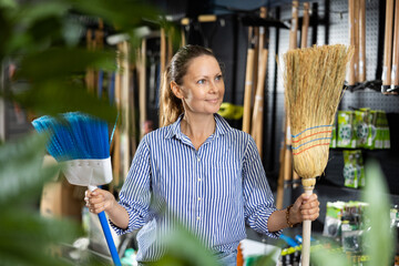 Middle-aged household female choosing between two brooms in a hardware store
