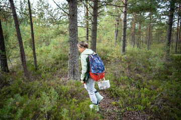 Female explorer collecting wild fungi in basket during hike along woodland with outdoor pack....