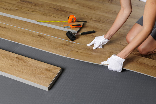 Woman installing SPC vinyl plank flooring with tools on underlayment