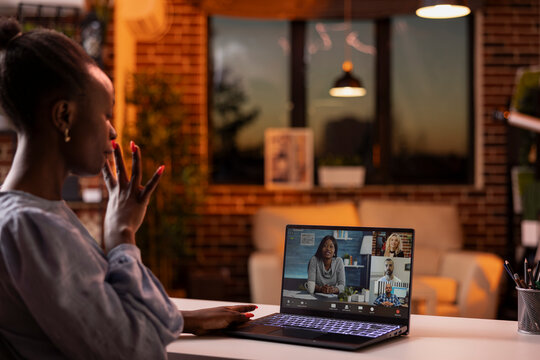 Black female freelancer seated at home office table, actively engaged in online business call. Young businesswoman presents strategies during video conference with remote team from cozy apartment.