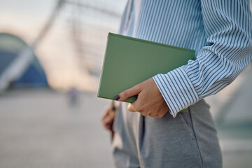 Businesswoman is holding a green book while standing in an urban area, possibly going to work or leaving the office