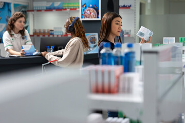 Obraz premium Dispensary asian woman reviewing drugs dosage on labels, reading the recommendation on medicine boxes before buying pills from the apothecary shelves. Medical supplies in a drugstore.