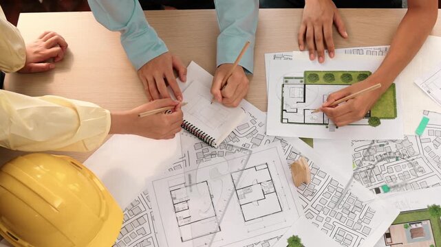 Architect and safety engineer discussion about building construction use blueprint on table with architectural document, measurement tool and wooden block scatter around at modern office. Delineation.