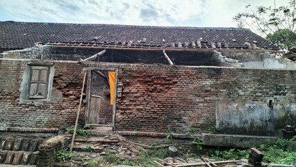 Photo of an old abandoned brick house with a broken roof, cracked walls, and rustic wooden door....