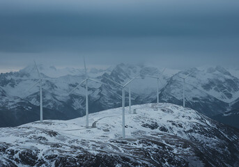 Wind Turbines on Snowy Mountain Ridge with Cloudy Sky
