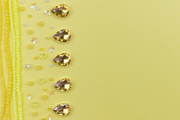 Beads crystals flower-shaped sequins and rhinestones frame on yellow background with copy space