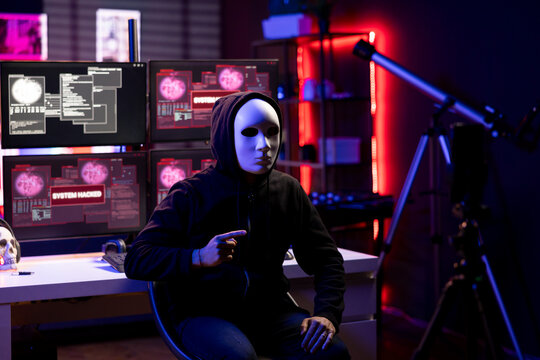 Masked man using phone to film video, doing espionage campaign from covert criminal den. Scammer wearing anonymous mask using smartphone to record demands from secret underground lair