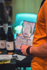 Person in an orange shirt holds an empty wine glass during a wine tasting event. Concept of wine, tasting, lifestyle centered around social gatherings and wine culture