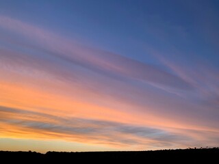 Beautiful colorful sunset sky with vibrant orange and purple clouds above dark forest silhouette
