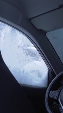 The driver stands outside cleaning snow from the car with a long-handled brush. He moves the brush from one side to the other. View from inside the car